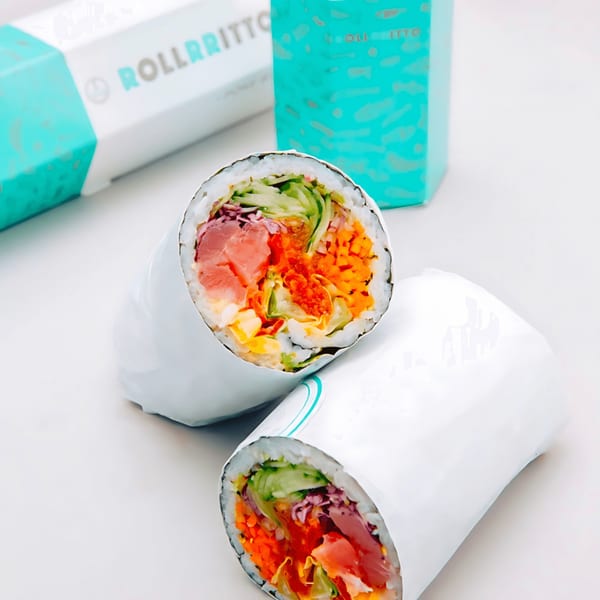 Two Rollrritto poke burritos, cut in half, showcasing fresh fish and vegetables, with branded packaging in the background.