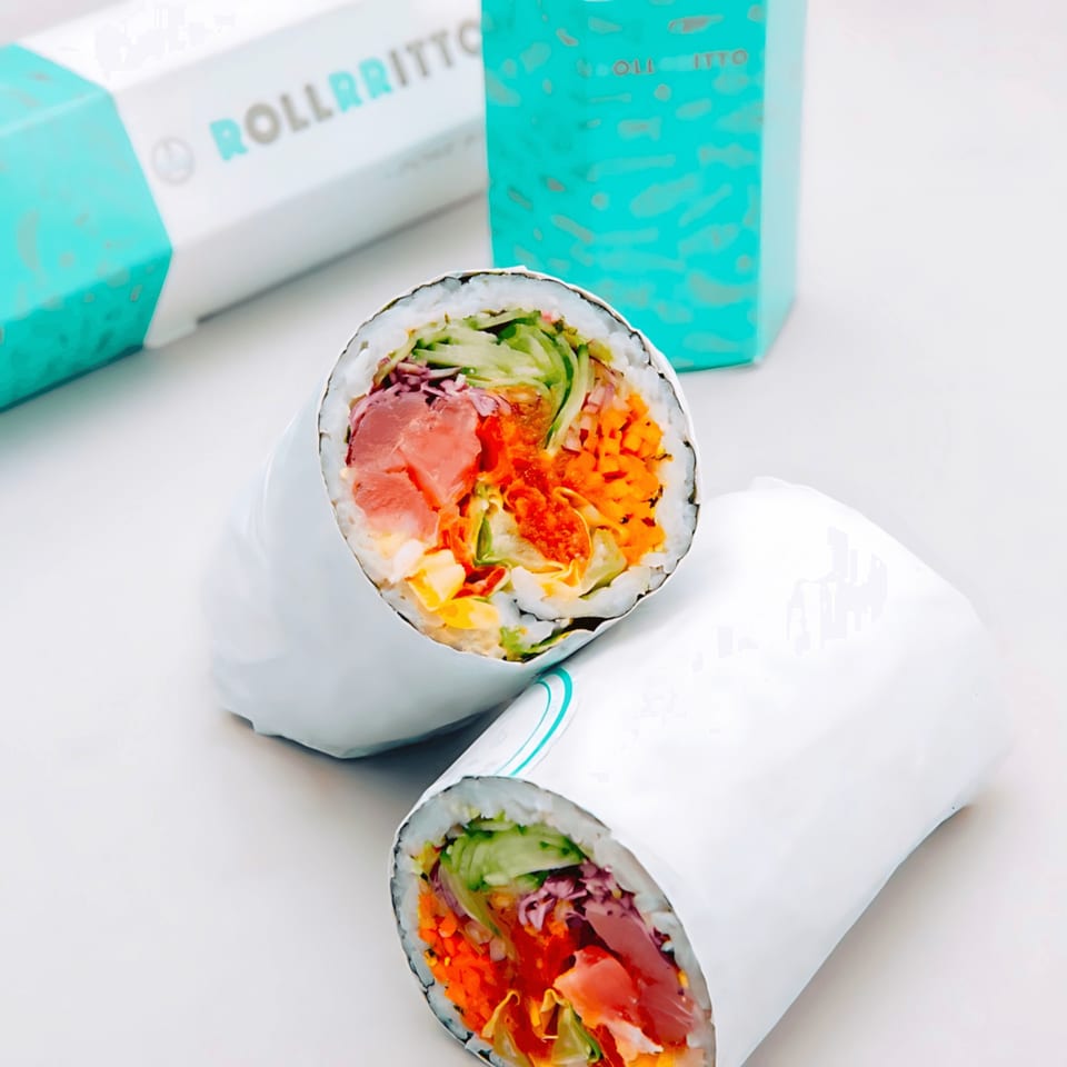 Two Rollrritto poke burritos, cut in half, showcasing fresh fish and vegetables, with branded packaging in the background.