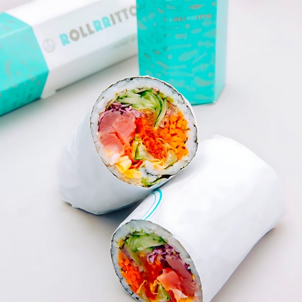 Two Rollrritto poke burritos, cut in half, showcasing fresh tuna, vegetables, and rice, with branded boxes.