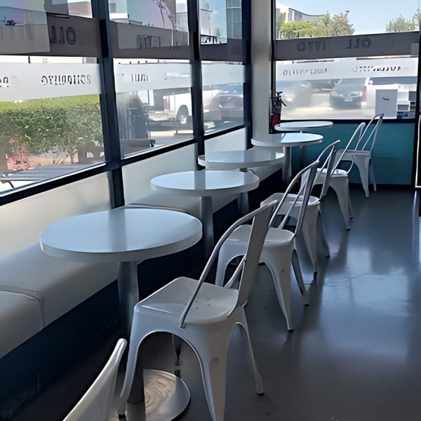 Interior of Rollrritto Poke Bar with white tables and chairs by large windows.