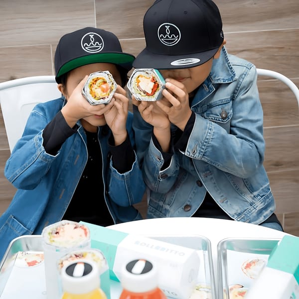 Two children in hats and denim jackets hold up Rollrritto poke burritos to their faces.